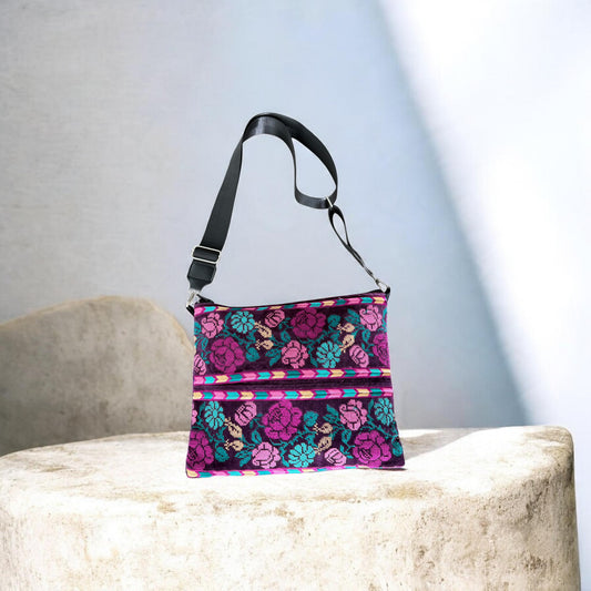 Banafsaj Crossbody with pink, purple and teal Palestinian Tatreez floral patterns and a black adjustable strap.