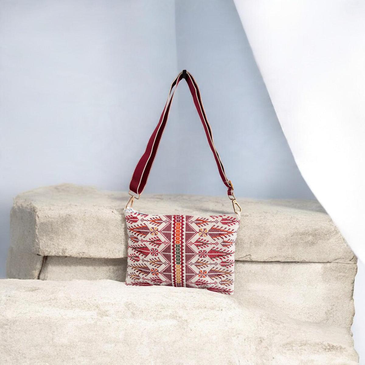 Cypress Tatreez Crossbody hanging by its burgundy strap, with red cypress motifs and a central multicolored band.