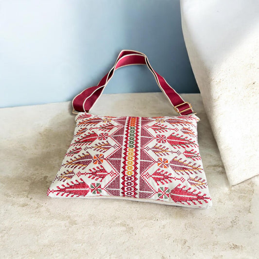 Angled front view of Cypress Tatreez Crossbody with burgundy strap, red cypress motifs and a multicolored central band.