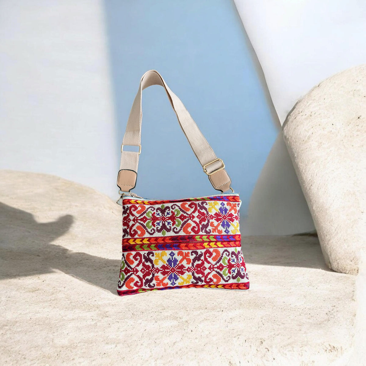 Qamar Crossbody with multicolor floral embroidery on a cream background, red patterned bands, and a beige adjustable strap.