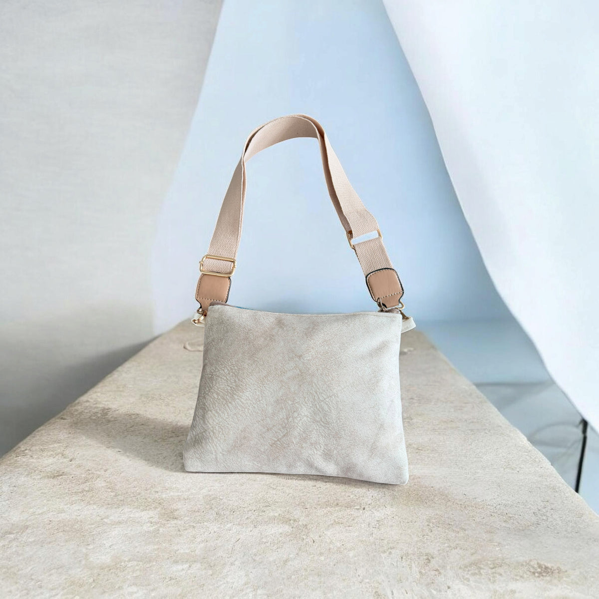 Rear view of Qamar Crossbody showing a plain cream back and beige adjustable strap with metal clips.”