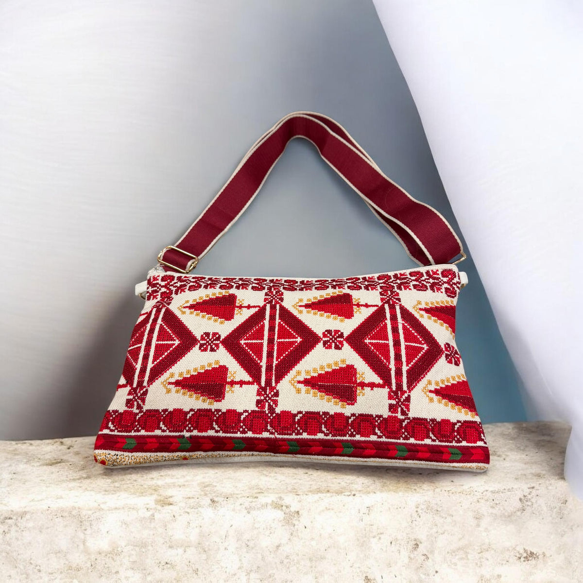 Sarw Crossbody with red Palestinian Tatreez cypress and diamond motifs on cream fabric and a burgundy strap.