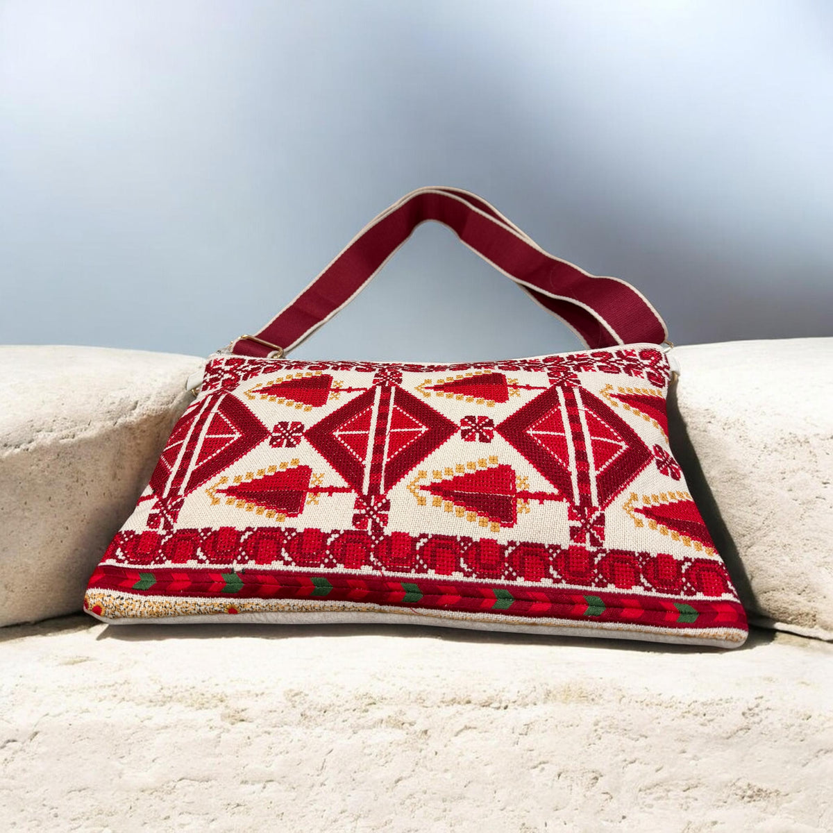 Sarw Crossbody resting between stone blocks, showing red and gold Tatreez motifs and a burgundy strap.