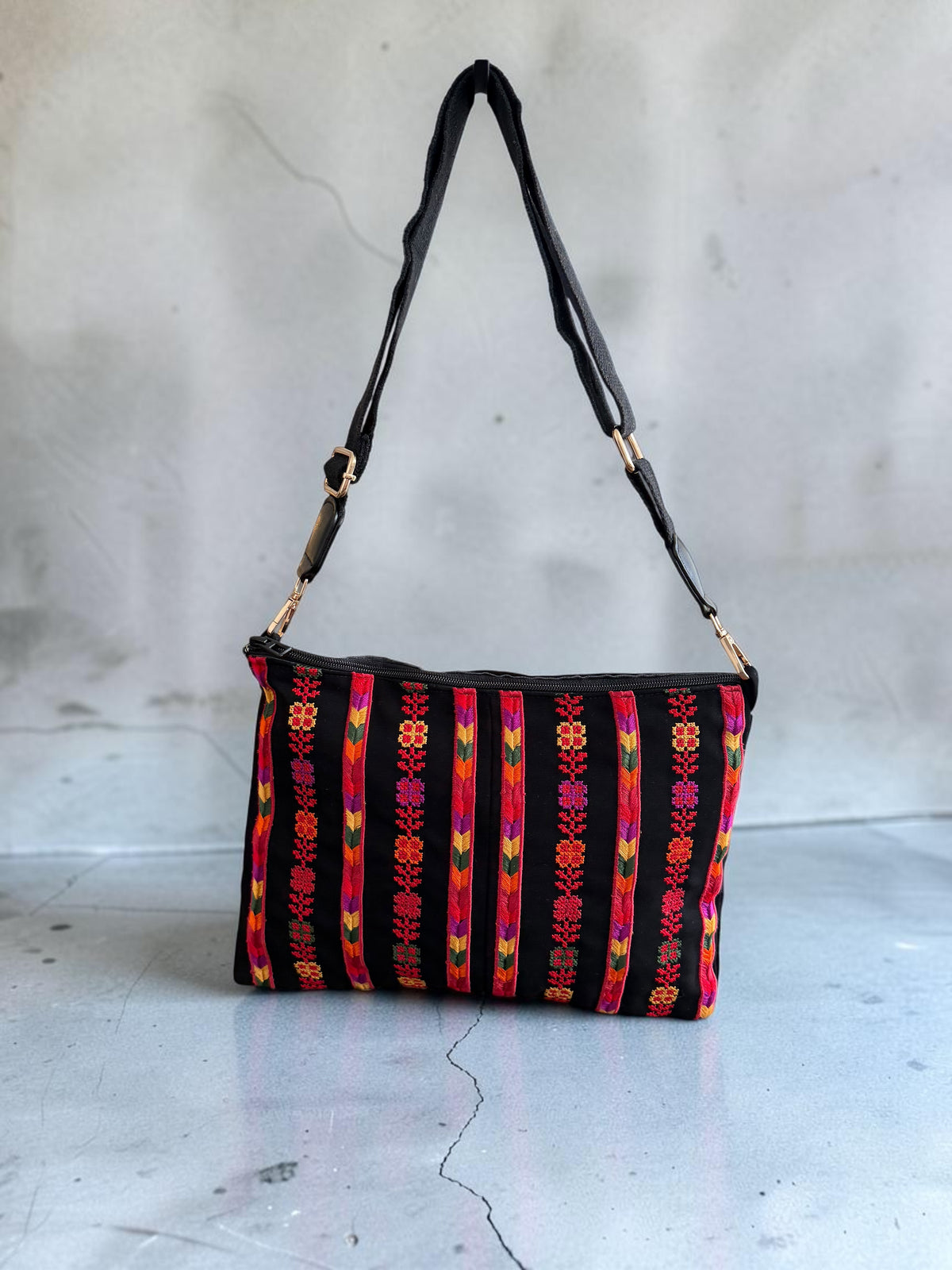 Nafnoof Crossbody with its black strap extended, showing colorful vertical Tatreez floral embroidery and a zip closure.